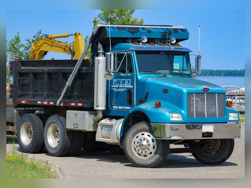 Blue Peterbilt dump truck at a work site with an excavator behind it